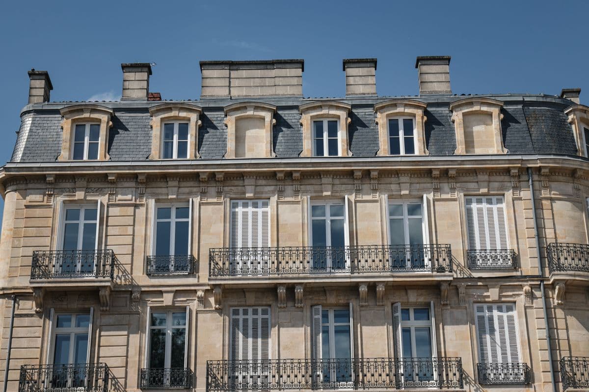 Façade d'immeuble en pierre blonde à Bordeaux, balcons en fer forgé et toit d'ardoise