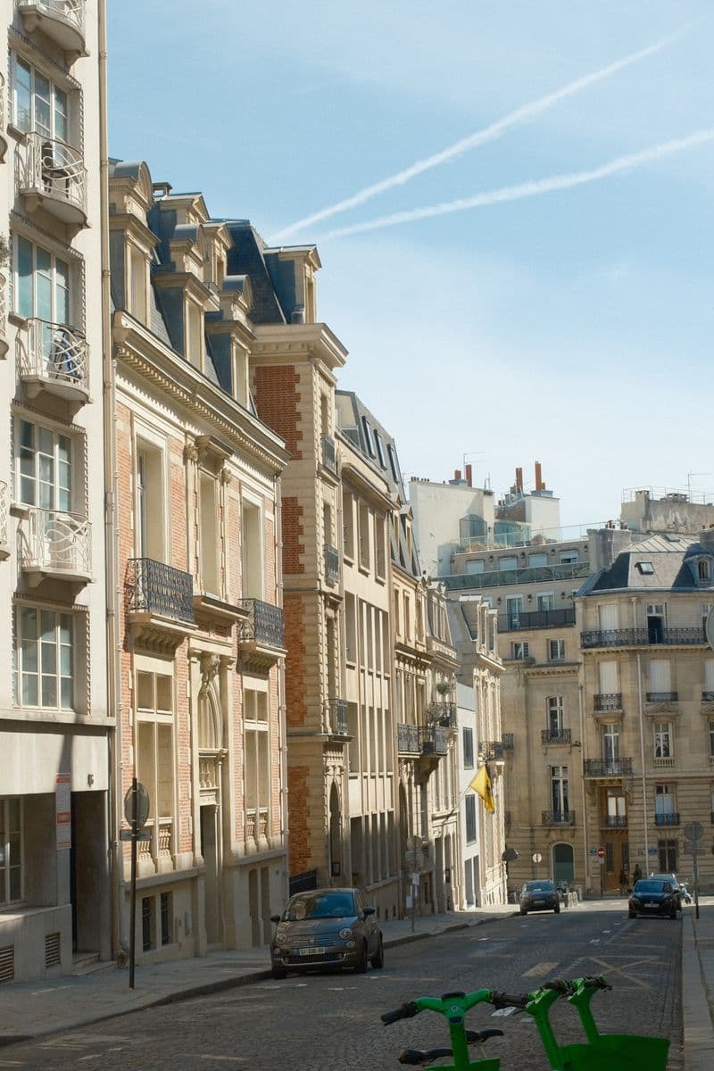 Rue parisienne le matin : immeubles en pierre, voitures garées et trottinettes