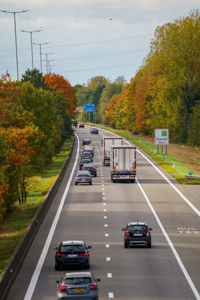 Voitures et camion sur une autoroute belge bordée d'arbres en automne
