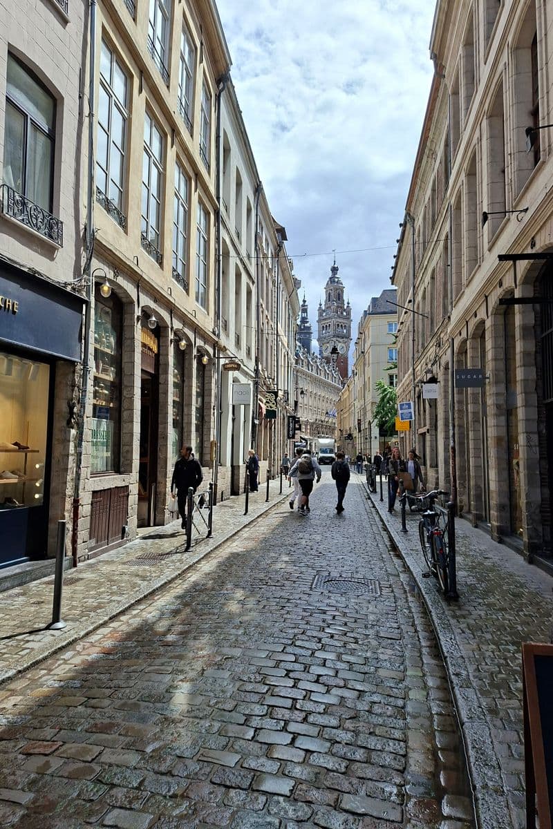 Rue pavée étroite de Lille bordée d'immeubles anciens, avec un clocher au fond