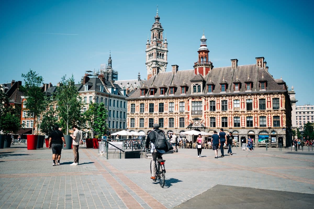 La Vieille Bourse et le beffroi de Lille, avec des passants et un cycliste sur la place