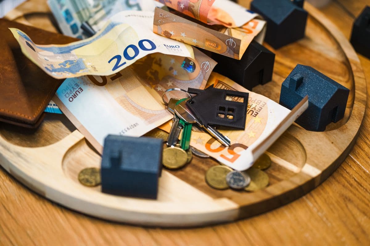 Billets en euros, clés et petites maisons miniatures sur un plateau en bois