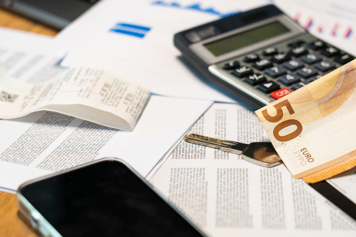 Calculatrice, billet de 50 euros, clé et documents posés sur un bureau