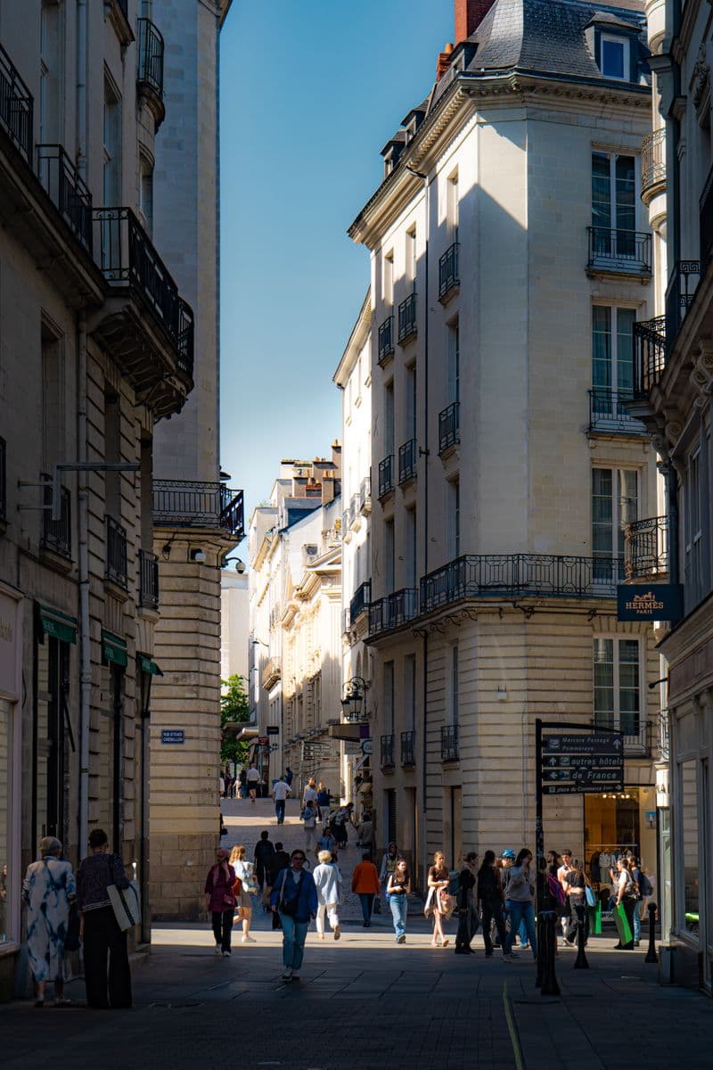 Rue du centre de Nantes entre des immeubles en pierre à balcons, avec des passants