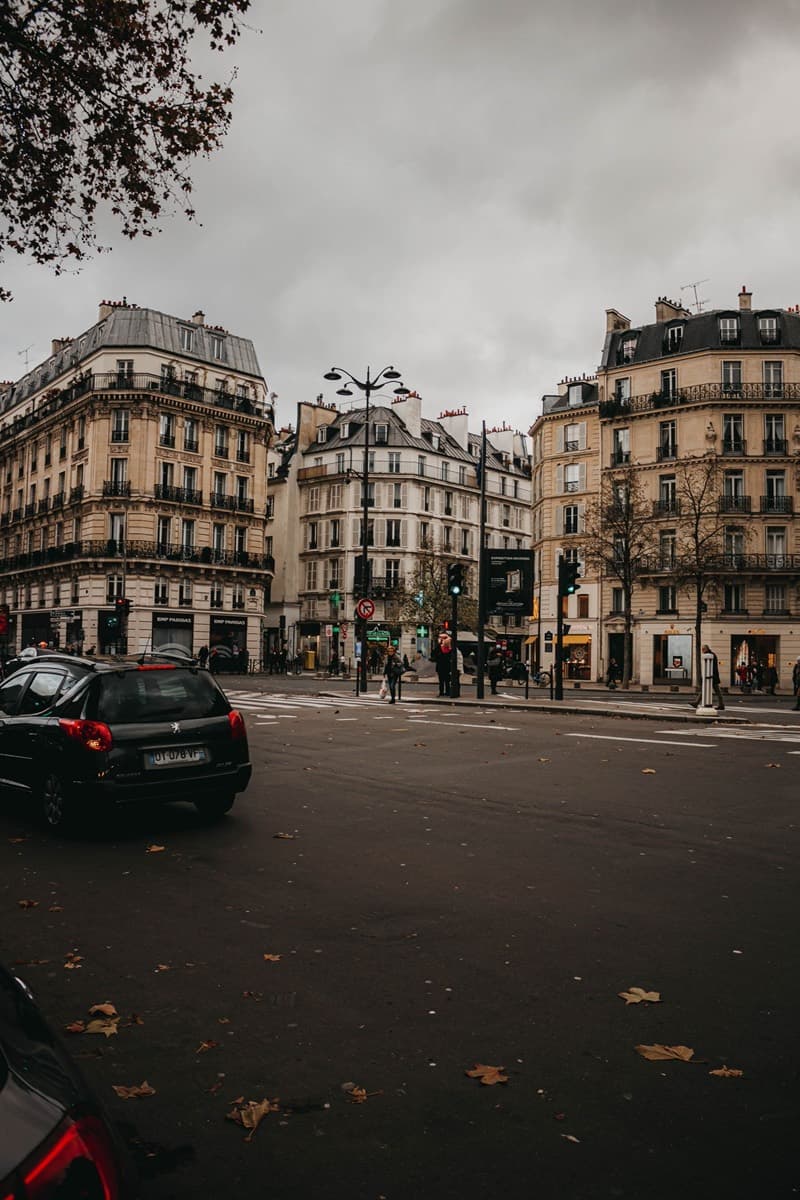 Carrefour parisien bordé d'immeubles haussmanniens, voitures garées le long du trottoir